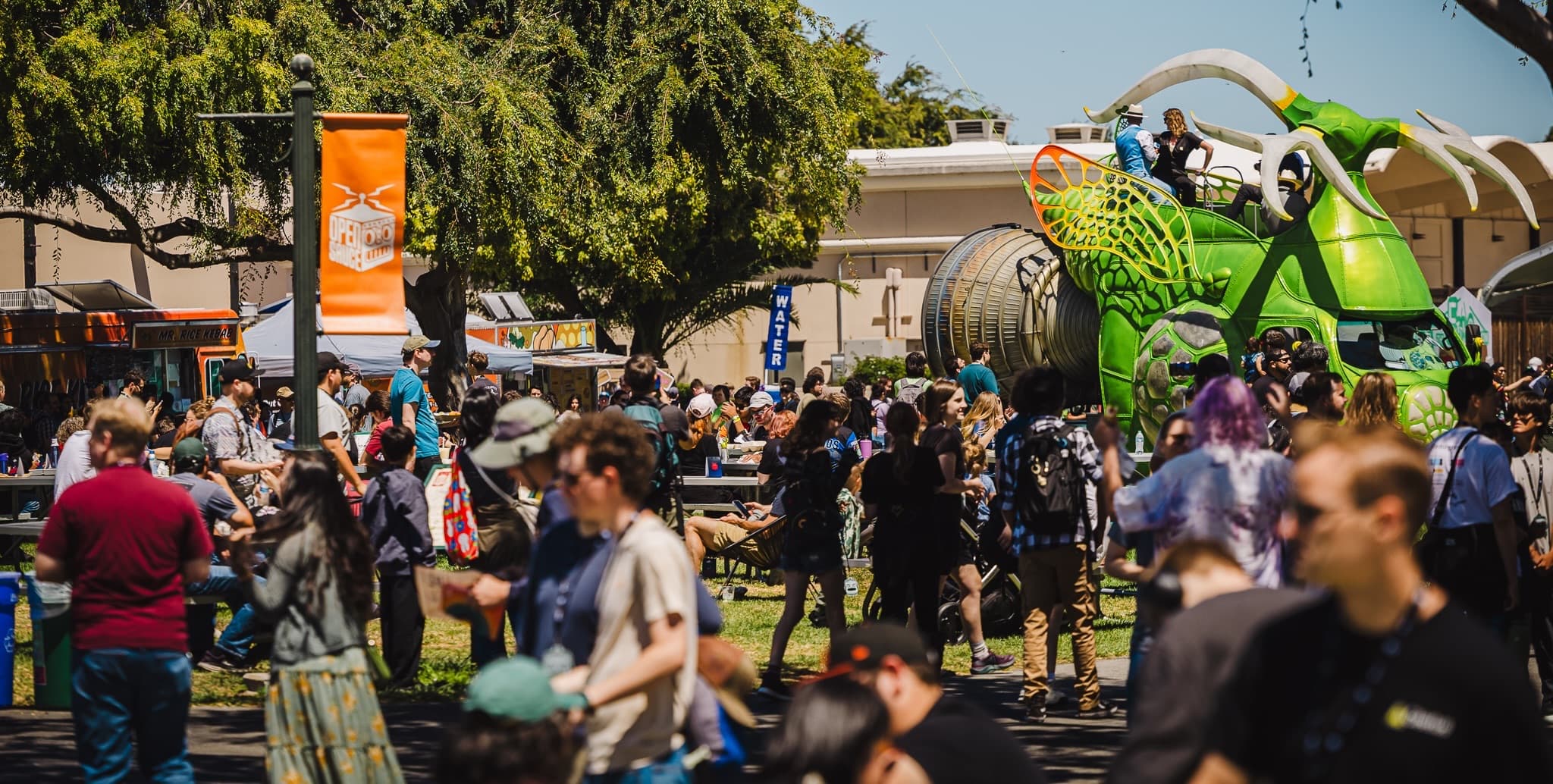Open Sauce festival grounds — crowd, food trucks, and a giant green mantis vehicle